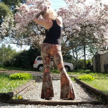 Load image into Gallery viewer, Feel sexy &amp; empower your inner femme fatale in these one of a kind flares! With the ultra high rise waist, these pants are ultra slimming, handcrafted in a unique liquid floral wave print, they feature a contrasting side stripe with golden pyramid studs. Fitted to the knees and flowing out into a super flared hem, just slip on these beauties and have fun mixing + matching them with all of our other knit styles as well as everything else in your wardrobe!
