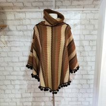 Load image into Gallery viewer, Like a good grounded hug, wrap yourself in this earthtone hooded poncho and you&#39;ll know what me mean! Handcrafted in a unique retro feel cotton crochet, this beautiful poncho features a nice solid feel hood to keep off the rain, quality weighted pom poms gracing the hemline and of course, leather heart elbow patches, your daily reminder that You are Loved!
