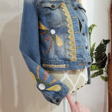 Load image into Gallery viewer, A complete labor of LOVE! This ONE OF A KIND upcycled denim jean jacket is sure to be your new favorite go-to. Featuring dragonfly inspired leather appliqued patchworks throughout the entire jacket in tones of yellow, mauve and earth. The unique vintage scalloped lace down the front and small crochet trim accents are highlighted with 10mm gold pyramid studs. You will also find our signature hand-embroidered &quot;LOVED&quot; script on the left sleeve at the cuff. Scoop up this beauty and feel loved everyday!
