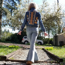 Load image into Gallery viewer, A complete labor of LOVE! This ONE OF A KIND upcycled denim jean jacket features hand appliqued tri-colored earth tone leather flowers throughout the entire jacket along with a &#39;Mayan Temple&#39; inspired design theme on the focal back feature. The unique vintage small crochet trim and center back exquisitely embroidered motif is a delight to the eye having an architectural feel strengthened by the 10mm gold pyramid studs. You will also find our signature hand-embroidered &quot;LOVED&quot; script on the right sleeve.
