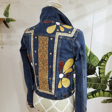 Load image into Gallery viewer, A complete labor of LOVE! This ONE OF A KIND upcycled denim jean jacket features hand appliqued tri-colored earth tone leather flowers throughout the entire jacket along with a &#39;Mayan Temple&#39; inspired design theme on the focal back feature. The unique vintage small crochet trim and center back exquisitely embroidered motif is a delight to the eye having an architectural feel strengthened by the 10mm gold pyramid studs. You will also find our signature hand-embroidered &quot;LOVED&quot; script on the right sleeve.
