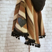 Load image into Gallery viewer, Like a good grounded hug, wrap yourself in this earthtone hooded poncho and you&#39;ll know what me mean! Handcrafted in a unique retro feel cotton crochet, this beautiful poncho features a nice solid feel hood to keep off the rain, quality weighted pom poms gracing the hemline and of course, leather heart elbow patches, your daily reminder that You are Loved!
