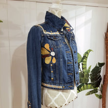 Load image into Gallery viewer, A complete labor of LOVE! This ONE OF A KIND upcycled denim jean jacket features hand appliqued tri-colored earth tone leather flowers throughout the entire jacket along with a &#39;Mayan Temple&#39; inspired design theme on the focal back feature. The unique vintage small crochet trim and center back exquisitely embroidered motif is a delight to the eye having an architectural feel strengthened by the 10mm gold pyramid studs. You will also find our signature hand-embroidered &quot;LOVED&quot; script on the right sleeve.
