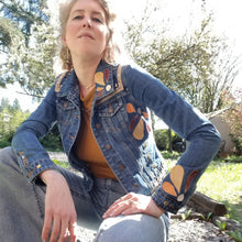 Load image into Gallery viewer, A complete labor of LOVE! This ONE OF A KIND upcycled denim jean jacket features hand appliqued tri-colored earth tone leather flowers throughout the entire jacket along with a &#39;Mayan Temple&#39; inspired design theme on the focal back feature. The unique vintage small crochet trim and center back exquisitely embroidered motif is a delight to the eye having an architectural feel strengthened by the 10mm gold pyramid studs. You will also find our signature hand-embroidered &quot;LOVED&quot; script on the right sleeve.
