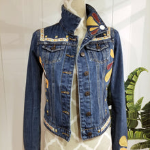 Load image into Gallery viewer, A complete labor of LOVE! This ONE OF A KIND upcycled denim jean jacket features hand appliqued tri-colored earth tone leather flowers throughout the entire jacket along with a &#39;Mayan Temple&#39; inspired design theme on the focal back feature. The unique vintage small crochet trim and center back exquisitely embroidered motif is a delight to the eye having an architectural feel strengthened by the 10mm gold pyramid studs. You will also find our signature hand-embroidered &quot;LOVED&quot; script on the right sleeve.
