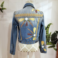 Load image into Gallery viewer, A complete labor of LOVE! This ONE OF A KIND upcycled denim jean jacket is sure to be your new favorite go-to. Featuring dragonfly inspired leather appliqued patchworks throughout the entire jacket in tones of yellow, mauve and earth. The unique vintage scalloped lace down the front and small crochet trim accents are highlighted with 10mm gold pyramid studs. You will also find our signature hand-embroidered &quot;LOVED&quot; script on the left sleeve at the cuff. Scoop up this beauty and feel loved everyday!
