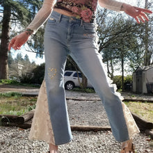 Load image into Gallery viewer, A completely upcycled LEVI denim crop flare jean featuring the sweetest country daisy cotton crochet lace with scalloping along the edges set in a unique asymmetrical detailing, gold + silver hand appliqued studded heart motifs, a one sided cotton eyelet trimmed side seam and 2 of our hand-embroidered LOVED scripts in soft pastel tones of gold, ivory and pink. Scoop up these beauties and feel loved everyday!
