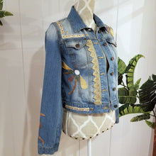 Load image into Gallery viewer, A complete labor of LOVE! This ONE OF A KIND upcycled denim jean jacket is sure to be your new favorite go-to. Featuring dragonfly inspired leather appliqued patchworks throughout the entire jacket in tones of yellow, mauve and earth. The unique vintage scalloped lace down the front and small crochet trim accents are highlighted with 10mm gold pyramid studs. You will also find our signature hand-embroidered &quot;LOVED&quot; script on the left sleeve at the cuff. Scoop up this beauty and feel loved everyday!
