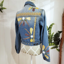 Load image into Gallery viewer, A complete labor of LOVE! This ONE OF A KIND upcycled denim jean jacket is sure to be your new favorite go-to. Featuring dragonfly inspired leather appliqued patchworks throughout the entire jacket in tones of yellow, mauve and earth. The unique vintage scalloped lace down the front and small crochet trim accents are highlighted with 10mm gold pyramid studs. You will also find our signature hand-embroidered &quot;LOVED&quot; script on the left sleeve at the cuff. Scoop up this beauty and feel loved everyday!
