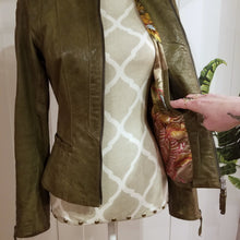 Load image into Gallery viewer, A complete labor of LOVE! This olive green vintage Canadian Brand DANIER leather jacket has been upcycled with a whole lot of love, literally. The sleeve cuffs have been enhanced with a whole bunch of small appliqued leather hearts, twelve to be exact, so unique, and so incredibly One-of-a-Kind. Scoop up this beauty and feel loved everyday!
