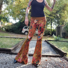 Load image into Gallery viewer, Feel sexy and empower your inner femme fatale in these one of a kind flares! With the ultra high rise waist, these pants are ultra slimming, handcrafted in a unique liquid floral wave print, they feature a contrasting side stripe with golden pyramid studs. Fitted to the knees and flowing out into a super flared hem, just slip on these beauties and have fun mixing + matching them with all of our other knit styles as well as everything else in your wardrobe!
