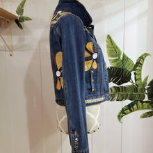 Load image into Gallery viewer, A complete labor of LOVE! This ONE OF A KIND upcycled denim jean jacket features hand appliqued tri-colored earth tone leather flowers throughout the entire jacket along with a &#39;Mayan Temple&#39; inspired design theme on the focal back feature. The unique vintage small crochet trim and center back exquisitely embroidered motif is a delight to the eye having an architectural feel strengthened by the 10mm gold pyramid studs. You will also find our signature hand-embroidered &quot;LOVED&quot; script on the right sleeve.
