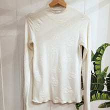 Load image into Gallery viewer, Simply said, this is a beauty, a classic on it&#39;s own or for layering! With the sweet fine ruffle edge finish throughout, this extra long sleeve top and gentle mock neck design will feel delightful on, handcrafted in a sumptuous off-white milky rose embossed print on an organic ever-so-soft cotton. Slip this beauty on and set the tone for the day!
