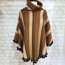 Load image into Gallery viewer, Like a good grounded hug, wrap yourself in this earthtone hooded poncho and you&#39;ll know what me mean! Handcrafted in a unique retro feel cotton crochet, this beautiful poncho features a nice solid feel hood to keep off the rain, quality weighted pom poms gracing the hemline and of course, leather heart elbow patches, your daily reminder that You are Loved!
