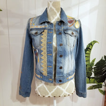 Load image into Gallery viewer, A complete labor of LOVE! This ONE OF A KIND upcycled denim jean jacket is sure to be your new favorite go-to. Featuring dragonfly inspired leather appliqued patchworks throughout the entire jacket in tones of yellow, mauve and earth. The unique vintage scalloped lace down the front and small crochet trim accents are highlighted with 10mm gold pyramid studs. You will also find our signature hand-embroidered &quot;LOVED&quot; script on the left sleeve at the cuff. Scoop up this beauty and feel loved everyday!
