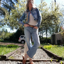 Load image into Gallery viewer, A complete labor of LOVE! This ONE OF A KIND upcycled denim jean jacket is sure to be your new favorite go-to. Featuring dragonfly inspired leather appliqued patchworks throughout the entire jacket in tones of yellow, mauve and earth. The unique vintage scalloped lace down the front and small crochet trim accents are highlighted with 10mm gold pyramid studs. You will also find our signature hand-embroidered &quot;LOVED&quot; script on the left sleeve at the cuff. Scoop up this beauty and feel loved everyday!
