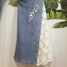 Load image into Gallery viewer, A completely upcycled LEVI denim crop flare jean featuring the sweetest country daisy cotton crochet lace with scalloping along the edges set in a unique asymmetrical detailing, gold + silver hand appliqued studded heart motifs, a one sided cotton eyelet trimmed side seam and 2 of our hand-embroidered LOVED scripts in soft pastel tones of gold, ivory and pink. Scoop up these beauties and feel loved everyday!
