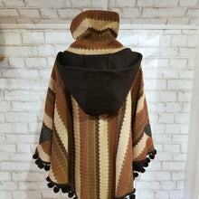 Load image into Gallery viewer, Like a good grounded hug, wrap yourself in this earthtone hooded poncho and you&#39;ll know what me mean! Handcrafted in a unique retro feel cotton crochet, this beautiful poncho features a nice solid feel hood to keep off the rain, quality weighted pom poms gracing the hemline and of course, leather heart elbow patches, your daily reminder that You are Loved!
