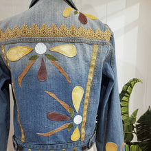 Load image into Gallery viewer, A complete labor of LOVE! This ONE OF A KIND upcycled denim jean jacket is sure to be your new favorite go-to. Featuring dragonfly inspired leather appliqued patchworks throughout the entire jacket in tones of yellow, mauve and earth. The unique vintage scalloped lace down the front and small crochet trim accents are highlighted with 10mm gold pyramid studs. You will also find our signature hand-embroidered &quot;LOVED&quot; script on the left sleeve at the cuff. Scoop up this beauty and feel loved everyday!
