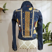 Load image into Gallery viewer, A complete labor of LOVE! This ONE OF A KIND upcycled denim jean jacket features hand appliqued tri-colored earth tone leather flowers throughout the entire jacket along with a &#39;Mayan Temple&#39; inspired design theme on the focal back feature. The unique vintage small crochet trim and center back exquisitely embroidered motif is a delight to the eye having an architectural feel strengthened by the 10mm gold pyramid studs. You will also find our signature hand-embroidered &quot;LOVED&quot; script on the right sleeve.
