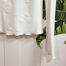 Load image into Gallery viewer, Simply said, this is a beauty, a classic on it&#39;s own or for layering! With the sweet fine ruffle edge finish throughout, this extra long sleeve top and gentle mock neck design will feel delightful on, handcrafted in a sumptuous off-white milky rose embossed print on an organic ever-so-soft cotton. Slip this beauty on and set the tone for the day!
