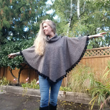 Load image into Gallery viewer, This is the perfect Fall Poncho to keep you warm + cozy. It features a tube collar to keep your neck warm + a contrasting black ribbed knit hood to keep the wind and raindrops off your hair. Made in a beautiful wool boucle it has a nice weighted feel and is a lovely piece to add a bit of warmth for the Fall/Winter season layered over your favorite sweaters, even your coats + jackets. The sides just cover the upper arms and the elbows which feature our &#39;signature&#39; heart shaped leather elbow patches with a fu
