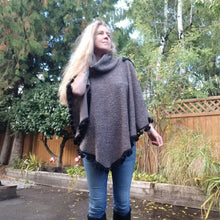 Load image into Gallery viewer, This is the perfect Fall Poncho to keep you warm + cozy. It features a tube collar to keep your neck warm + a contrasting black ribbed knit hood to keep the wind and raindrops off your hair. Made in a beautiful wool boucle it has a nice weighted feel and is a lovely piece to add a bit of warmth for the Fall/Winter season layered over your favorite sweaters, even your coats + jackets. The sides just cover the upper arms and the elbows which feature our &#39;signature&#39; heart shaped leather elbow patches with a fu
