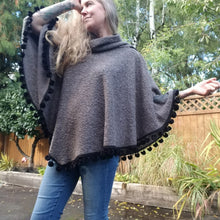 Load image into Gallery viewer, This is the perfect Fall Poncho to keep you warm + cozy. It features a tube collar to keep your neck warm + a contrasting black ribbed knit hood to keep the wind and raindrops off your hair. Made in a beautiful wool boucle it has a nice weighted feel and is a lovely piece to add a bit of warmth for the Fall/Winter season layered over your favorite sweaters, even your coats + jackets. The sides just cover the upper arms and the elbows which feature our &#39;signature&#39; heart shaped leather elbow patches with a fu
