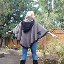 Load image into Gallery viewer, This is the perfect Fall Poncho to keep you warm + cozy. It features a tube collar to keep your neck warm + a contrasting black ribbed knit hood to keep the wind and raindrops off your hair. Made in a beautiful wool boucle it has a nice weighted feel and is a lovely piece to add a bit of warmth for the Fall/Winter season layered over your favorite sweaters, even your coats + jackets. The sides just cover the upper arms and the elbows which feature our &#39;signature&#39; heart shaped leather elbow patches with a fu
