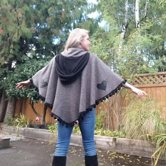 This is the perfect Fall Poncho to keep you warm + cozy. It features a tube collar to keep your neck warm + a contrasting black ribbed knit hood to keep the wind and raindrops off your hair. Made in a beautiful wool boucle it has a nice weighted feel and is a lovely piece to add a bit of warmth for the Fall/Winter season layered over your favorite sweaters, even your coats + jackets. The sides just cover the upper arms and the elbows which feature our 'signature' heart shaped leather elbow patches with a fu